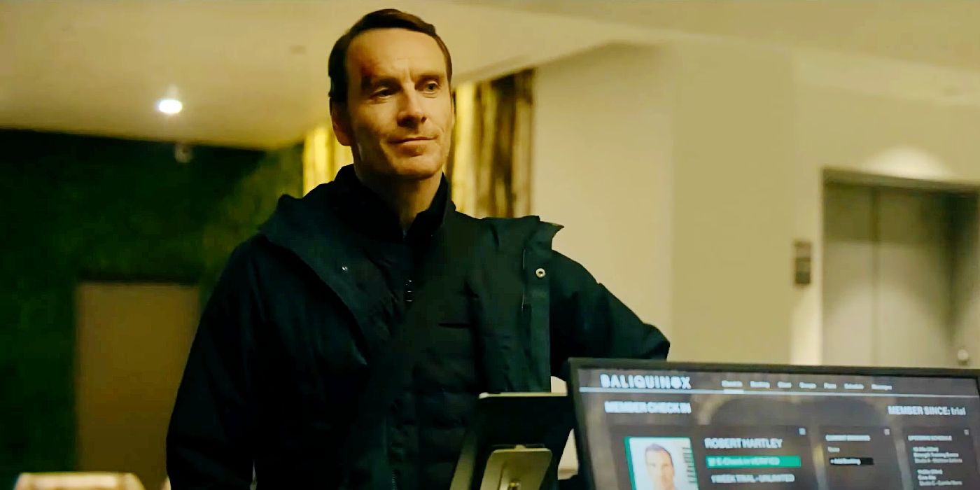 Michael Fassbender standing at a counter and smiling in The Killer.
