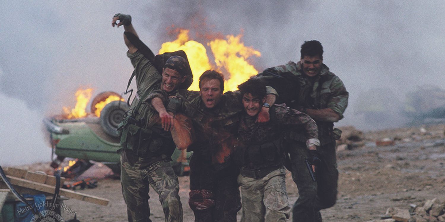 The cast of Navy SEALs rescuing a wounded combatant and running from a toppled car aflame