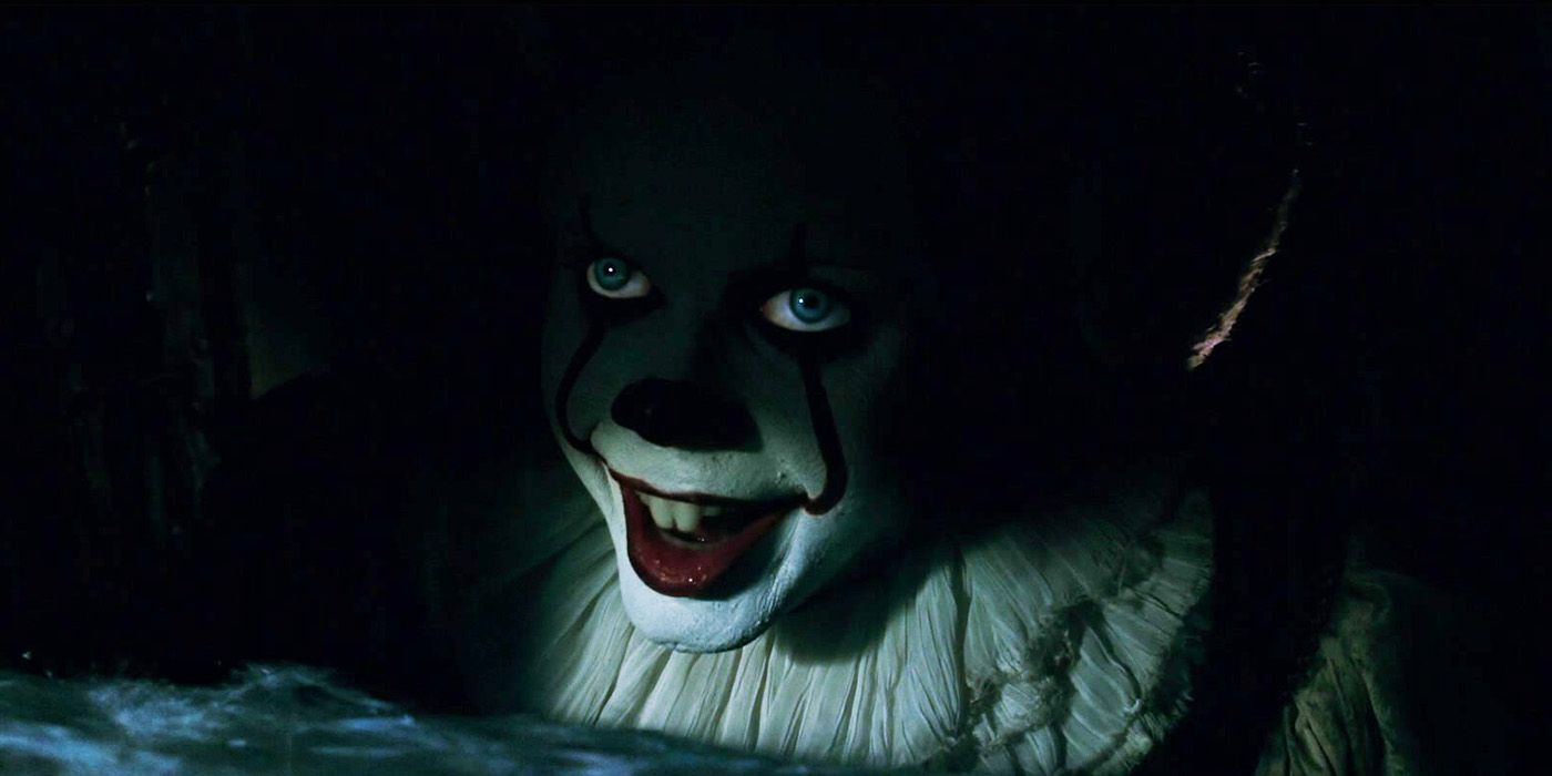 Bill Skarsgård's Pennywise smiling in the shadows of the drain in the 2017 horror movie It