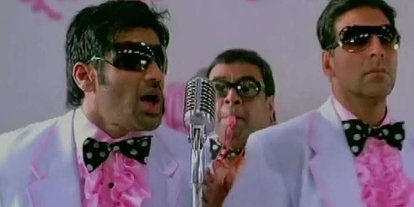 Raju, Shyam, and Babu all dressed up in white tuxedos and pink ties singing on a stage in Phir Hera Pheri.