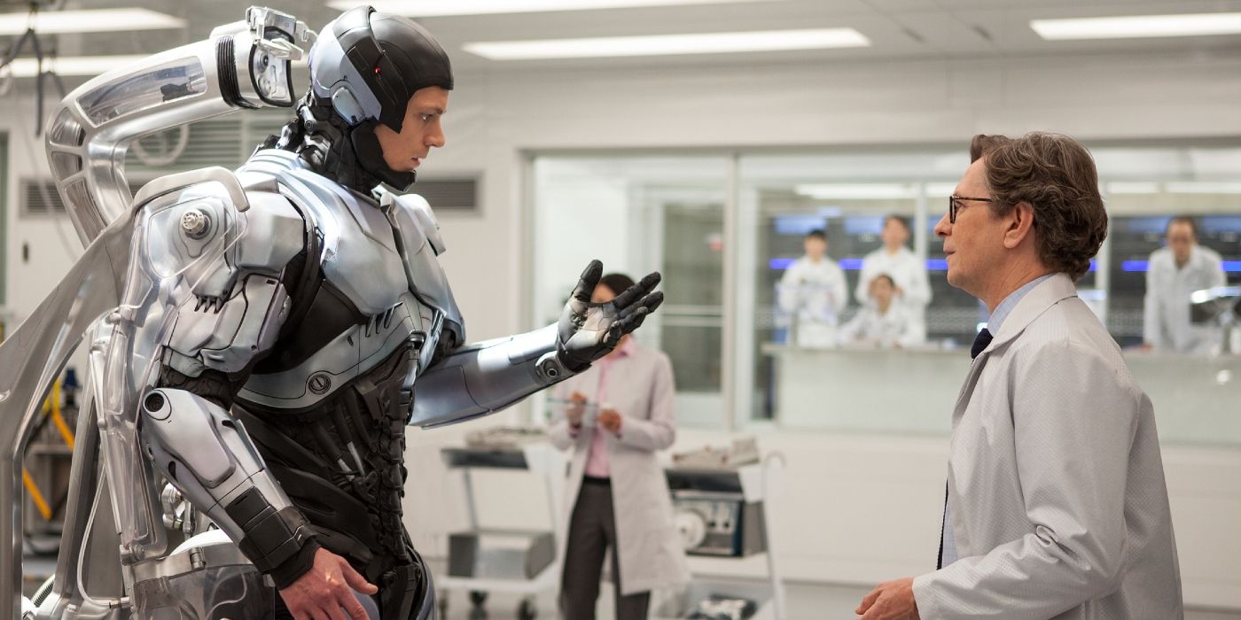 Joel Kinnamon looking at his robotic hand in front of Gary Oldman in 2014's RoboCop.