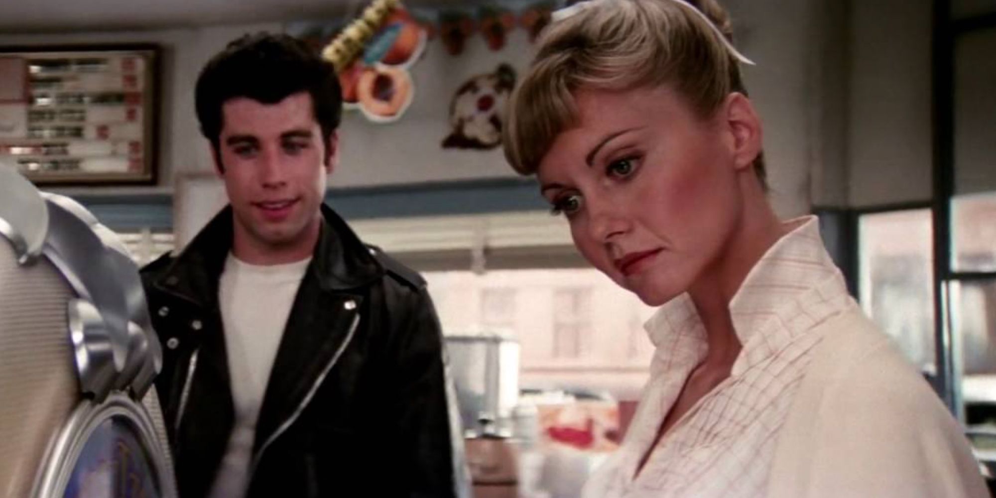 Sandy olhando para a jukebox enquanto Danny fica ao fundo em Grease