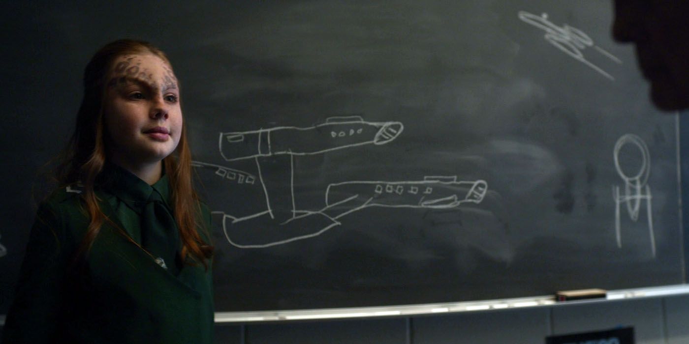 An alien child poses next to a crude chalkboard drawing of the Enterprise