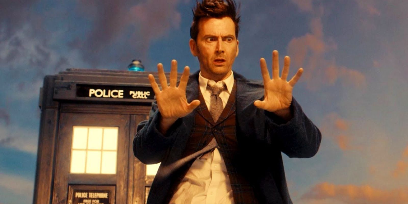 The Fourteenth Doctor looks at his hands while standing in front of the TARDIS in Doctor Who.