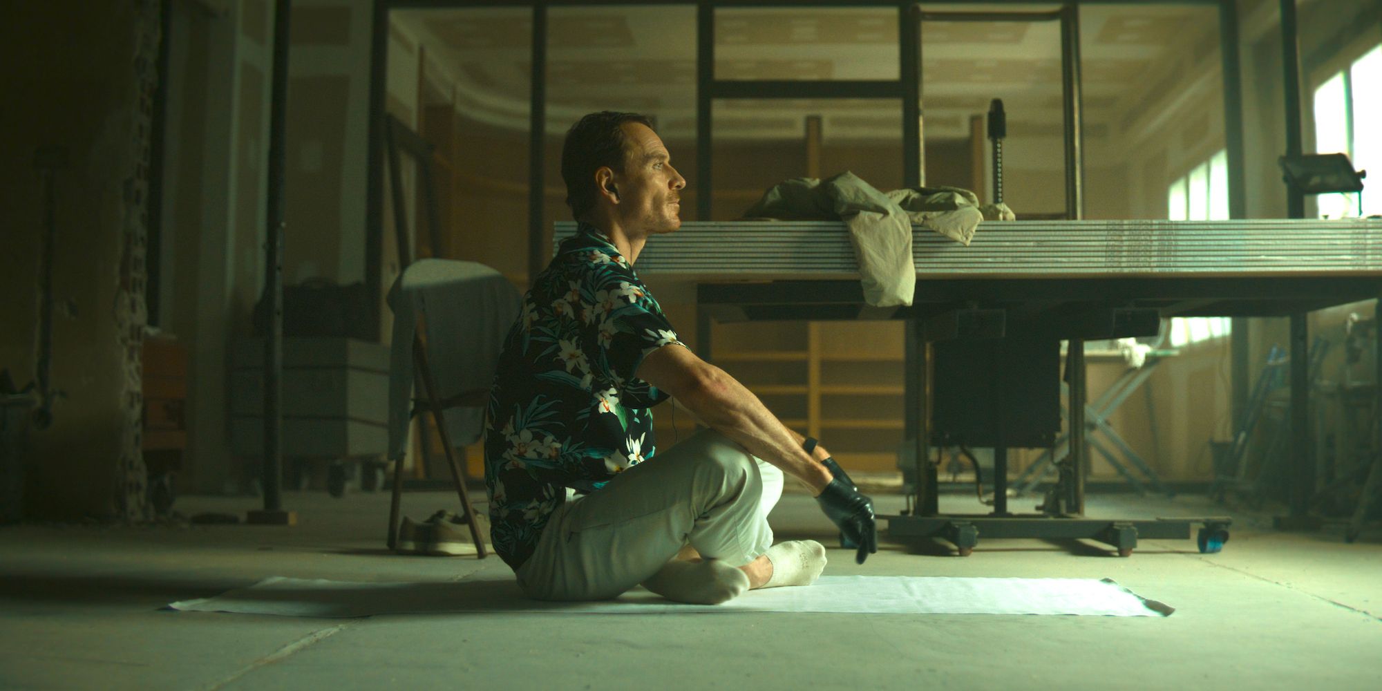 Michael Fassbender's unnamed assassin sitting on the floor with his legs crossed in a wework room in The Killer