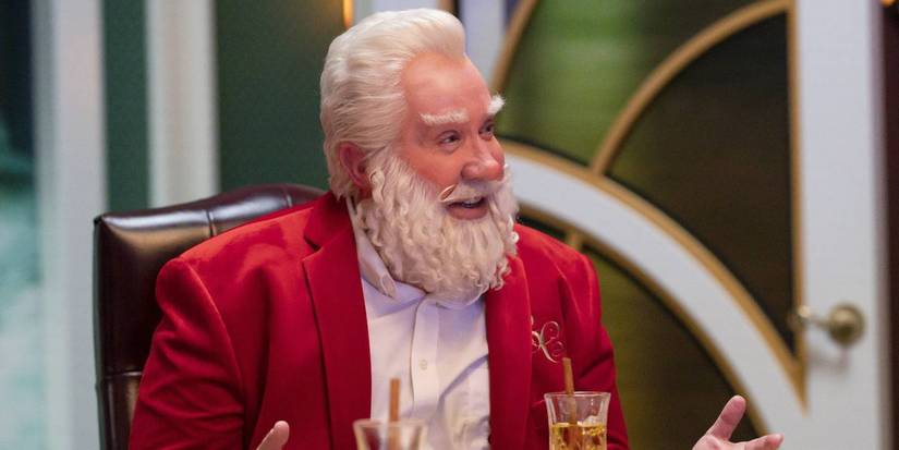 Scott Calvin (Tim Allen) sitting at a table and smiling in The Santa Clauses