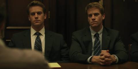 The Winklesvoss twins (Armie Hammer) sitting at a table in suits in The Social Network
