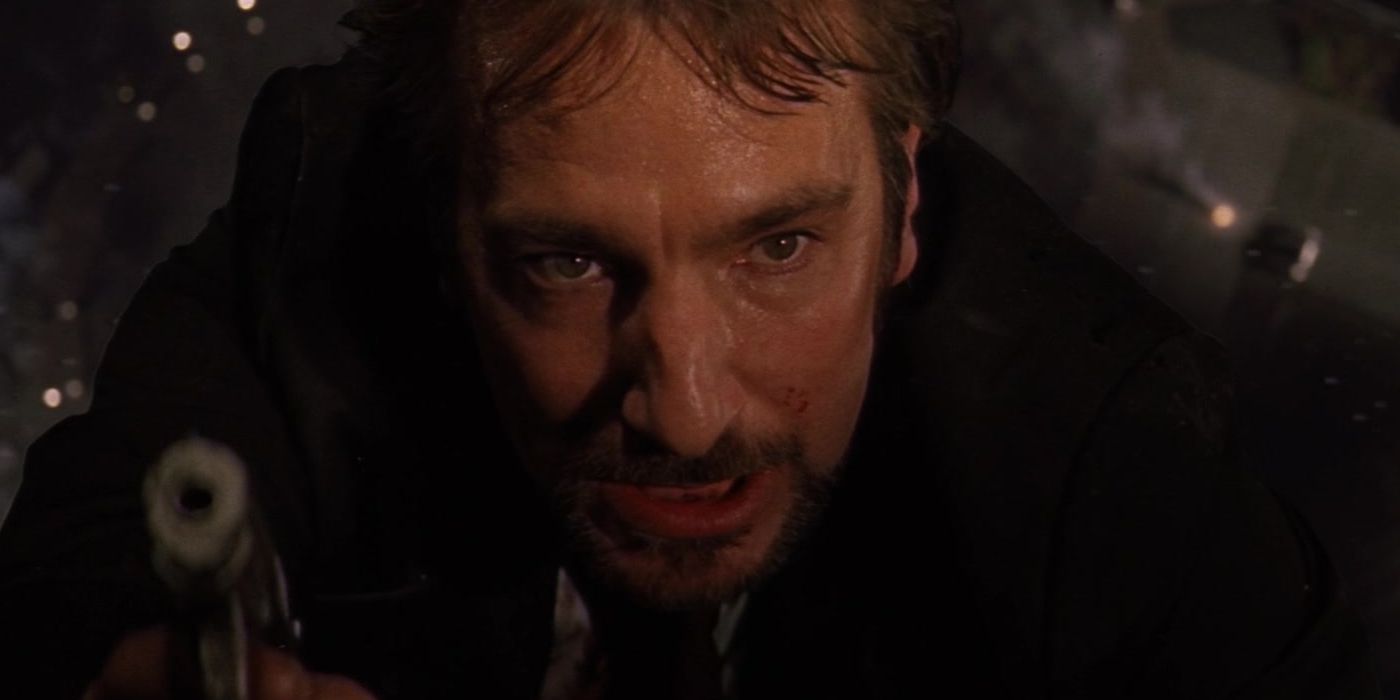 Alan Rickman como Hans Gruber apontando uma arma enquanto fica pendurado na janela em Die Hard