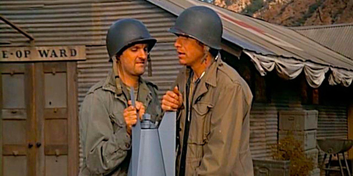 Alan Alda and Wayne Rogers stand over a dud bomb in a scene from MASH season 1
