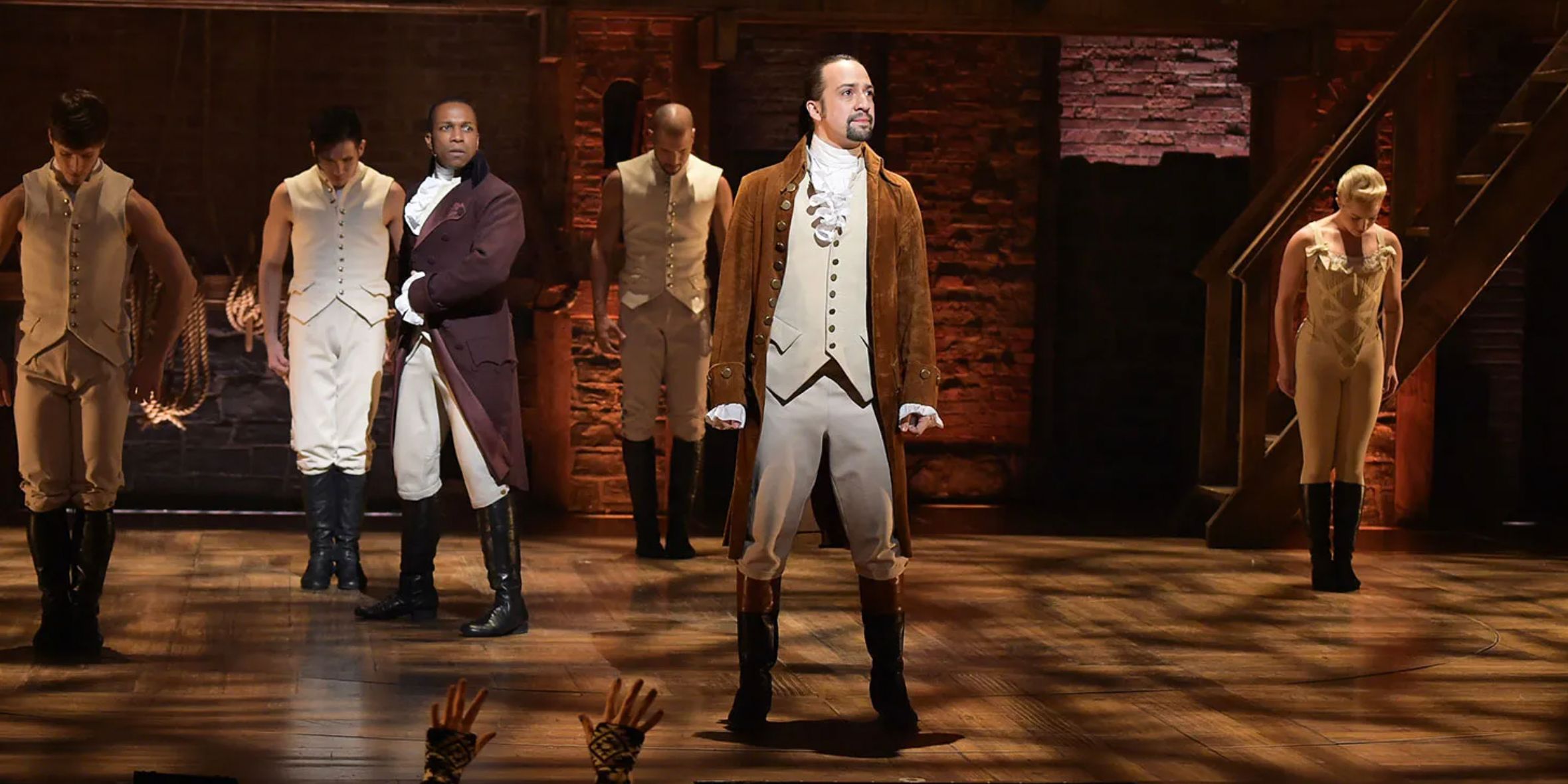 Alexander Hamilton no meio do palco com Aaron Burr e os membros da companhia atrás dele em Hamilton