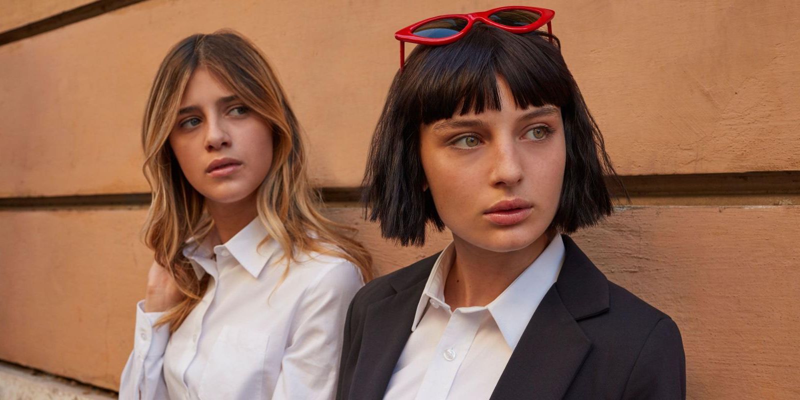 Chiara and Ludovica lean against a brown wall while looking off to the side in Netflix’s Baby.