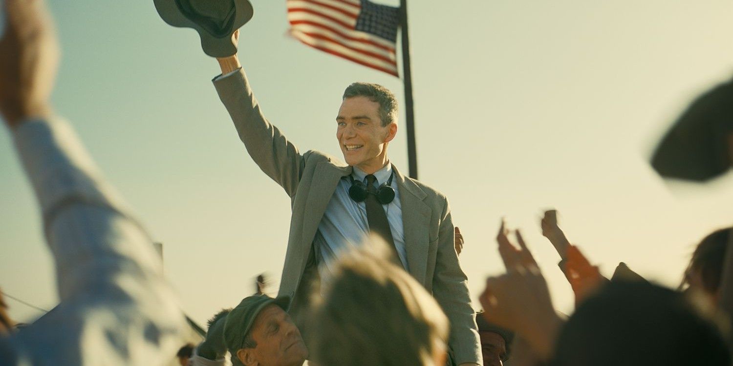 Cillian Murphy as Oppenheimer celebrating above a cheering crowd with the American flag in the background