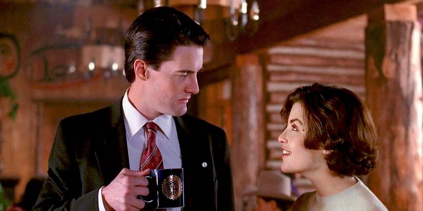 Dale (Kyle MacLachlan) and Audrey (Sherilyn Fenn) talking at the lodge in Twin Peaks. Cooper is holding a cup of coffee. 