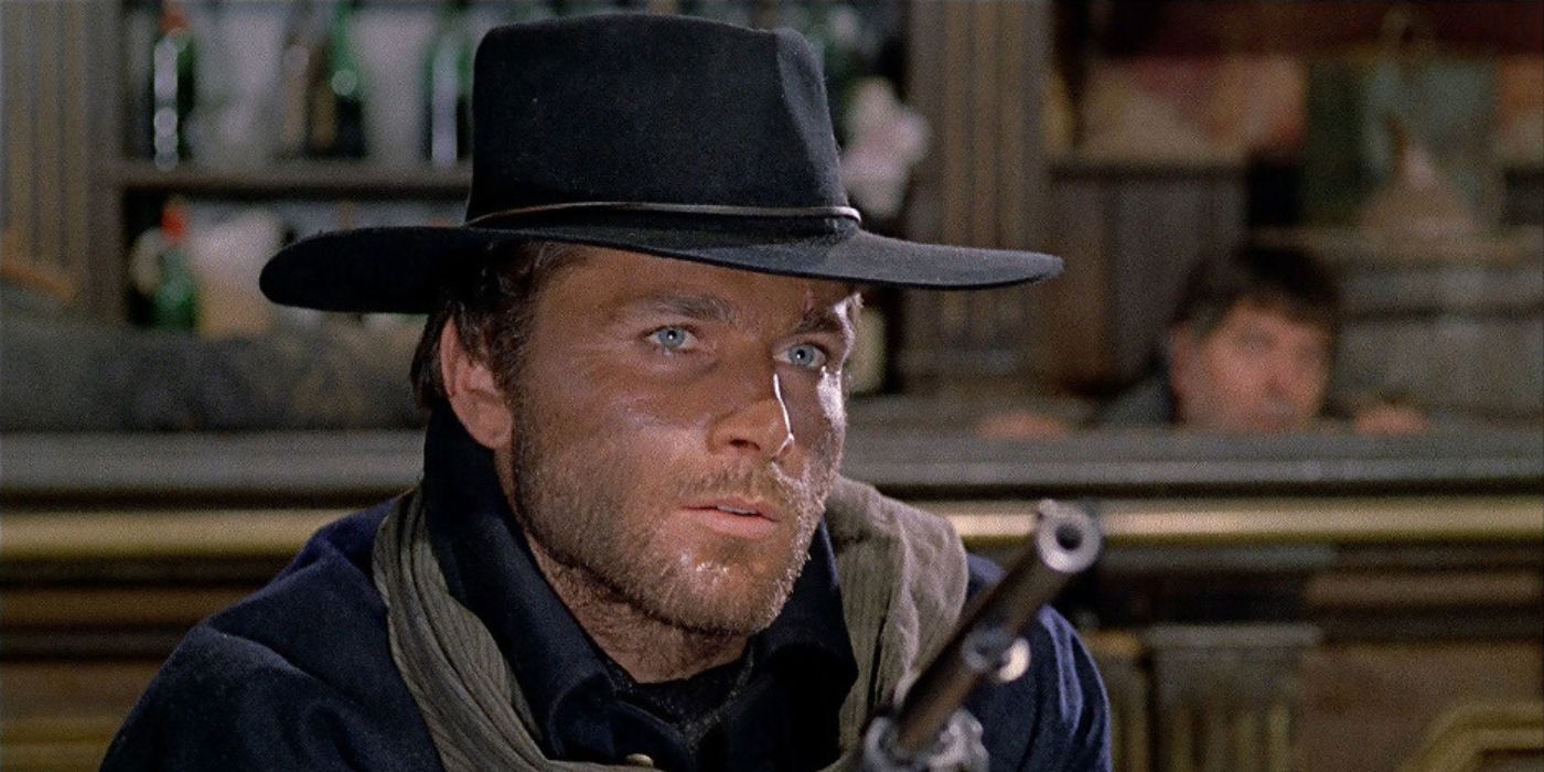 Django (Franco Nero) aims his revolver at a bandit while seated at a table inside a saloon