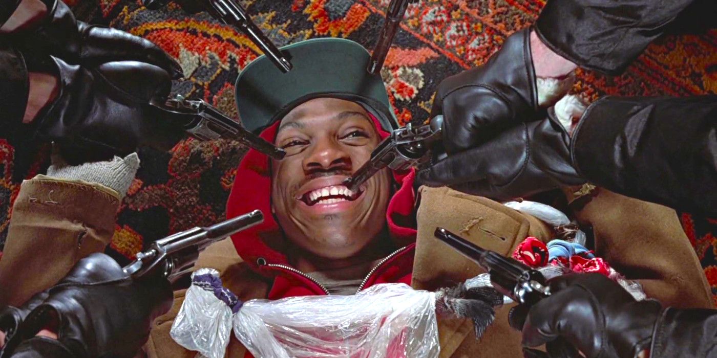 Eddie Murphy lies prone on a carpeted floor smiling upward while multiple guns are pointed at his face in Trading Places