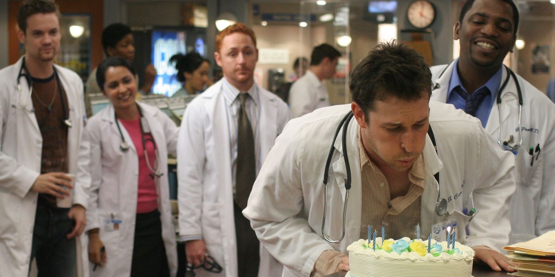 Carter blowing out candles on a cake with Neela and Morris behind him in ER season 11