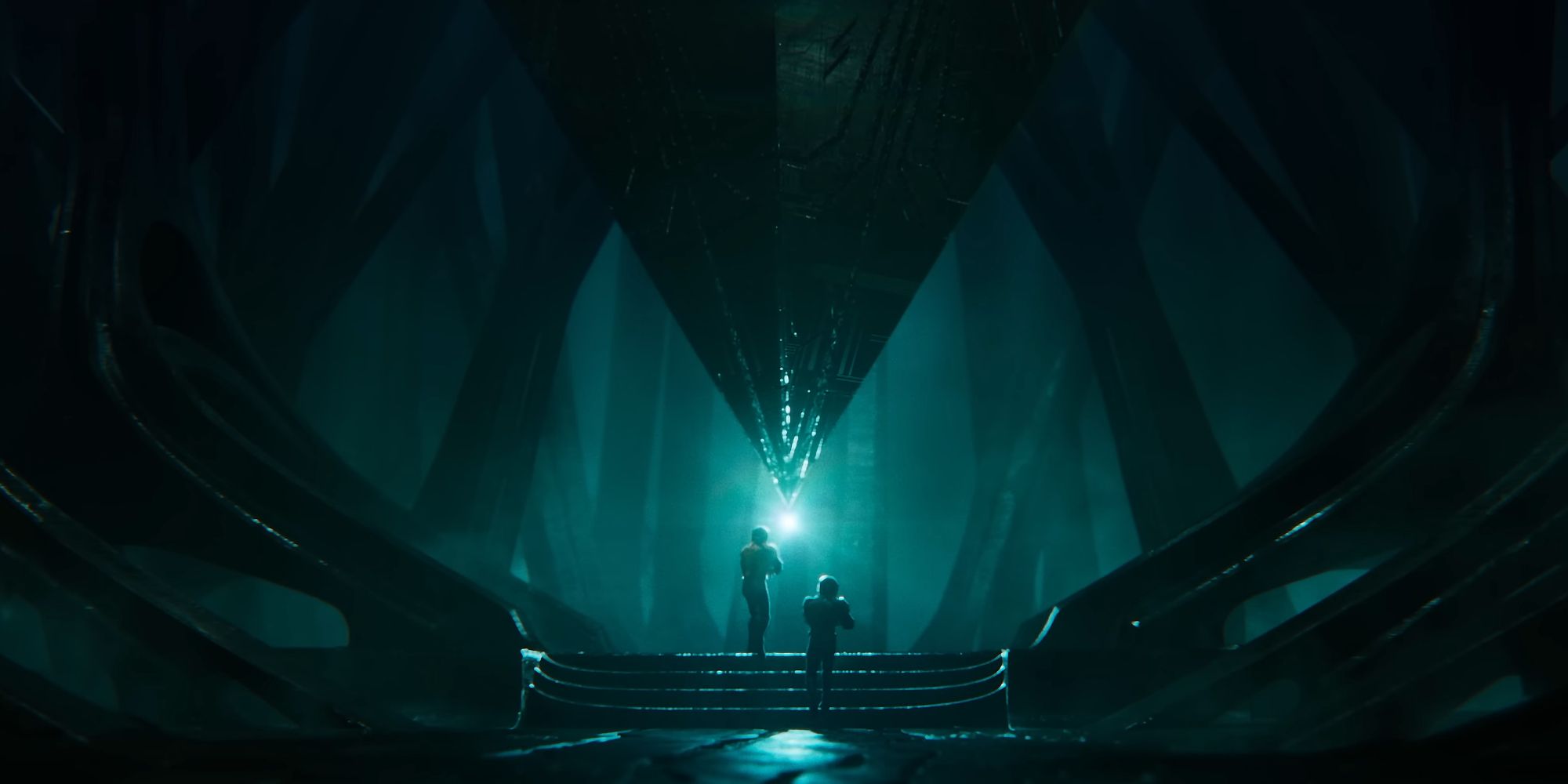 Two figures approaching a glowing object, surrounded by advanced alien technology.