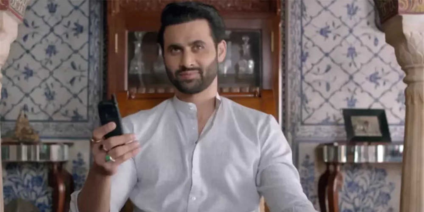 Freddy Daruwala as Home Minister smiling and holding up a phone in Inspector Avinash