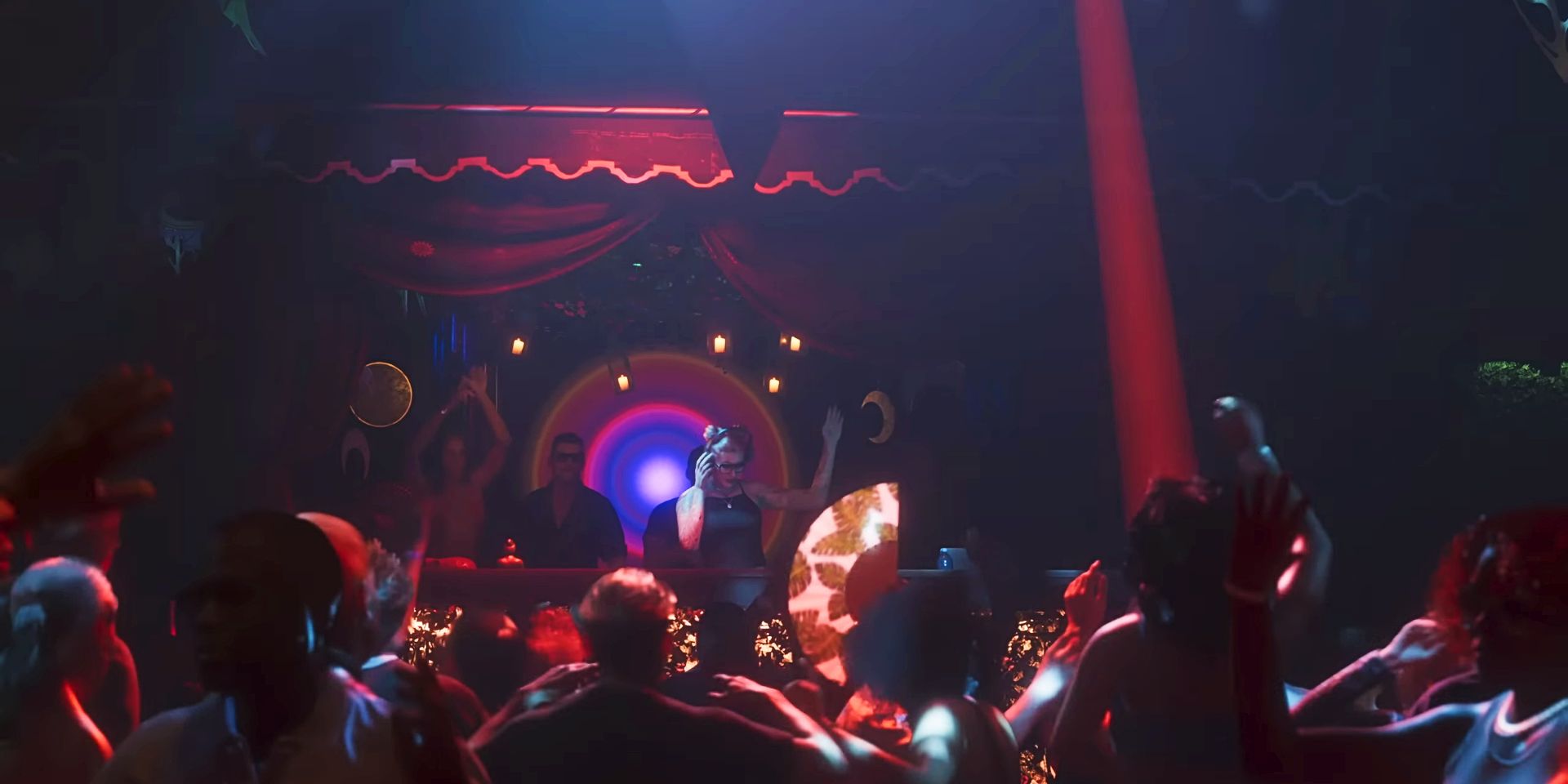 Una escena de club del tráiler de GTA 6.  Multitudes de gente bailando, mientras un DJ agarra sus auriculares y levanta un brazo en el aire.  Luces de neón y cortinas rojas adornan la pista de baile.