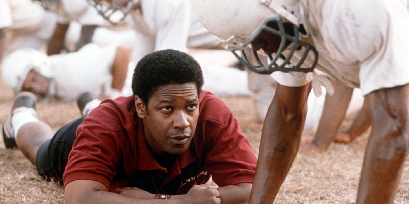 Herman Boone lying on the ground in front of his players coaching them in Remember the Titans. 
