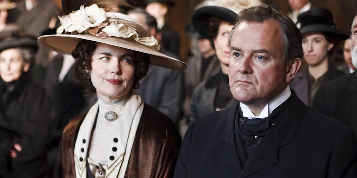 Cora is wearing a large hat and looking at Robert who is grimacing on Downton Abbey.