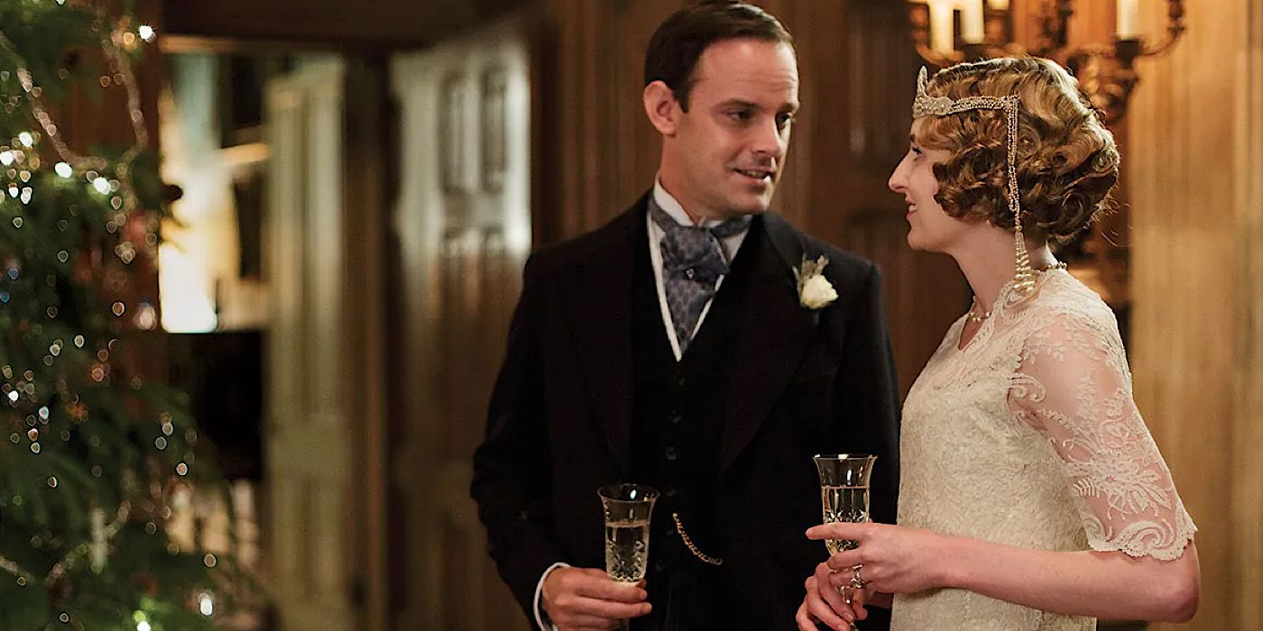 Edith and Bertie looking at each other and holding drinks next to a Christmas tree in Downton Abbey.