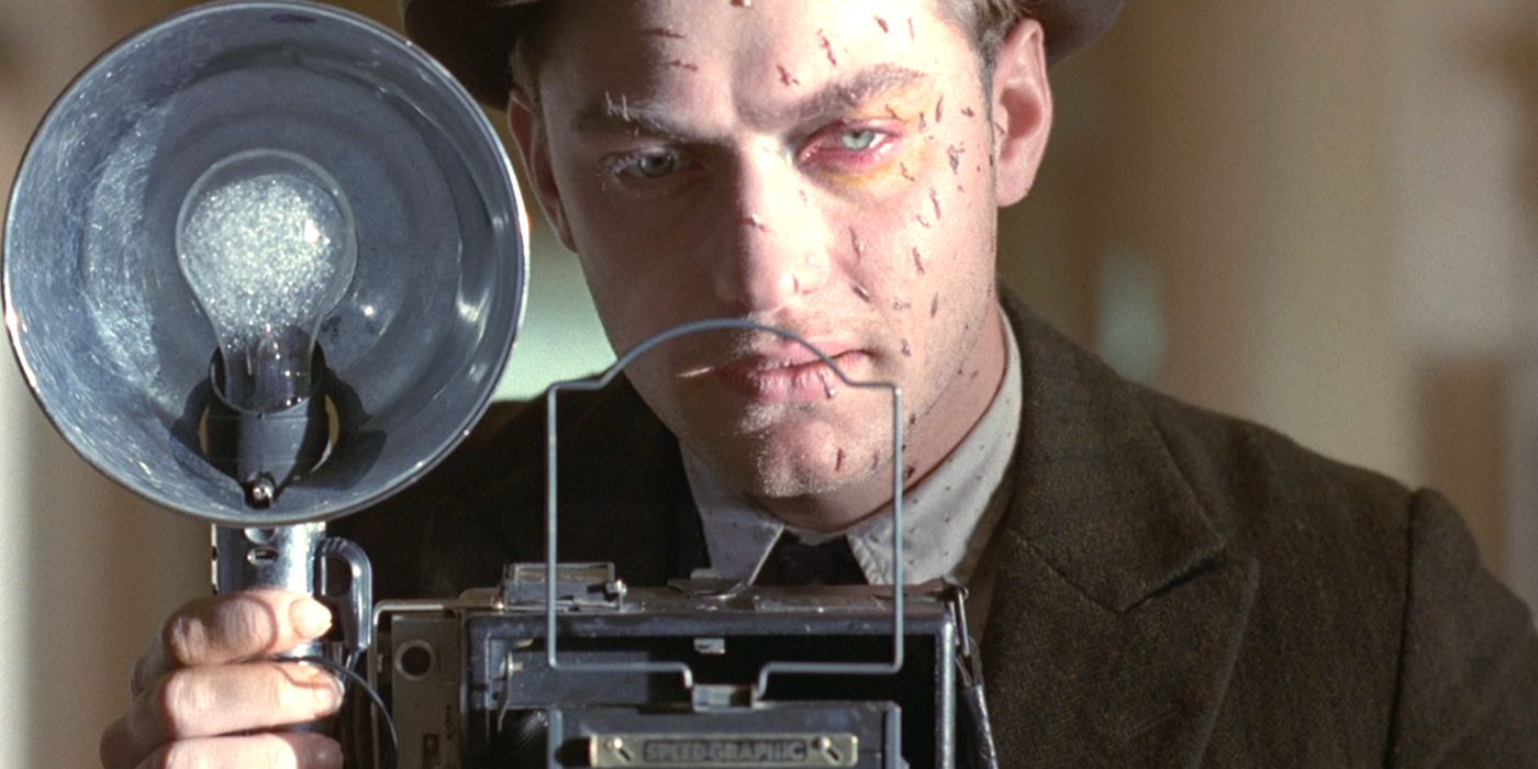 Jude Law with cuts on his face and a camera in Road to Perdition