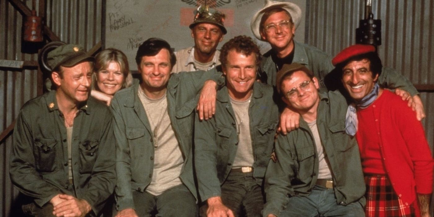 The cast of MASH from season 3 smiling and huddling for a photo in uniform
