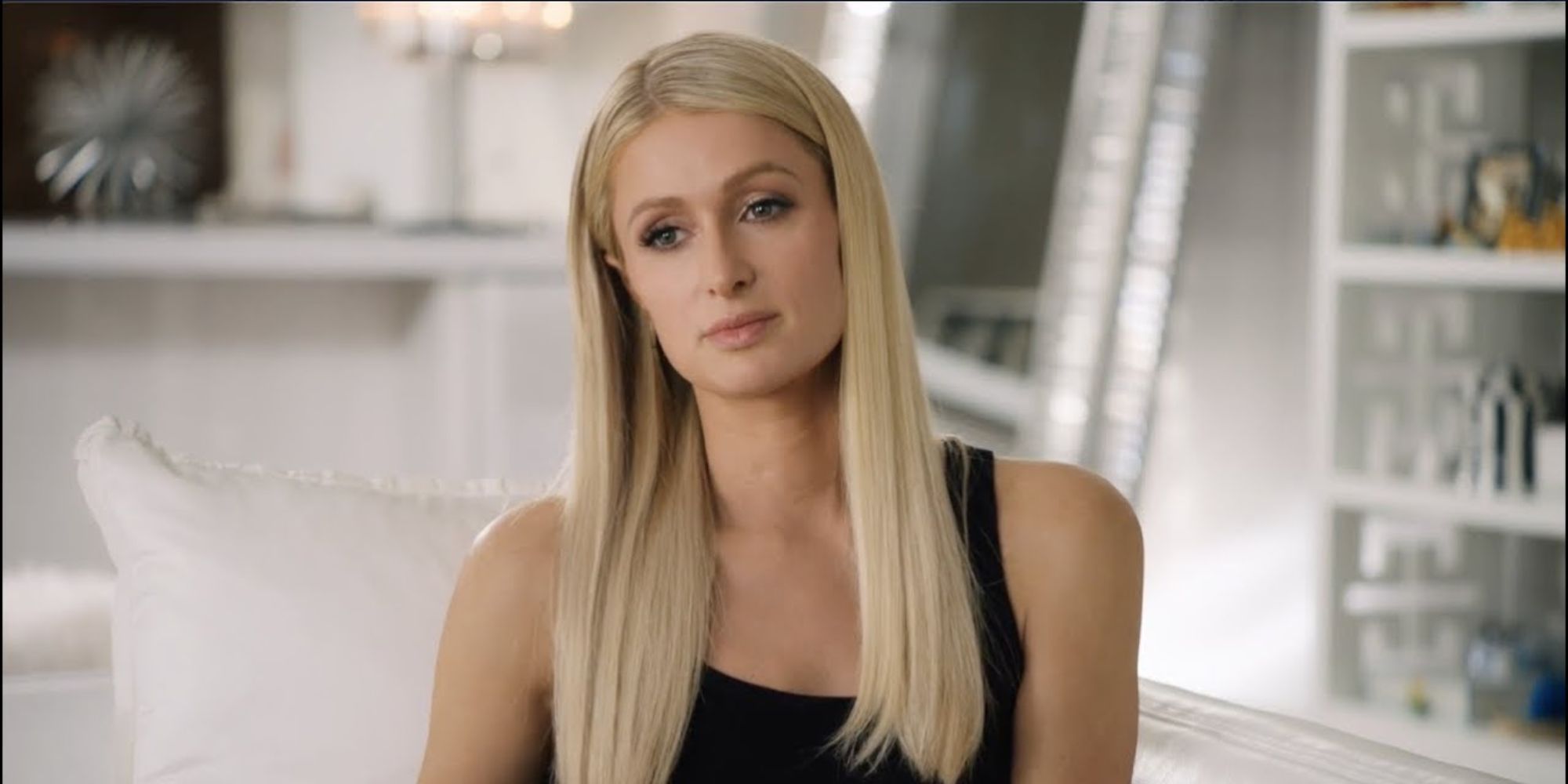 Paris Hilton is sitting on a couch in Netflix's Hell Camp documentary.