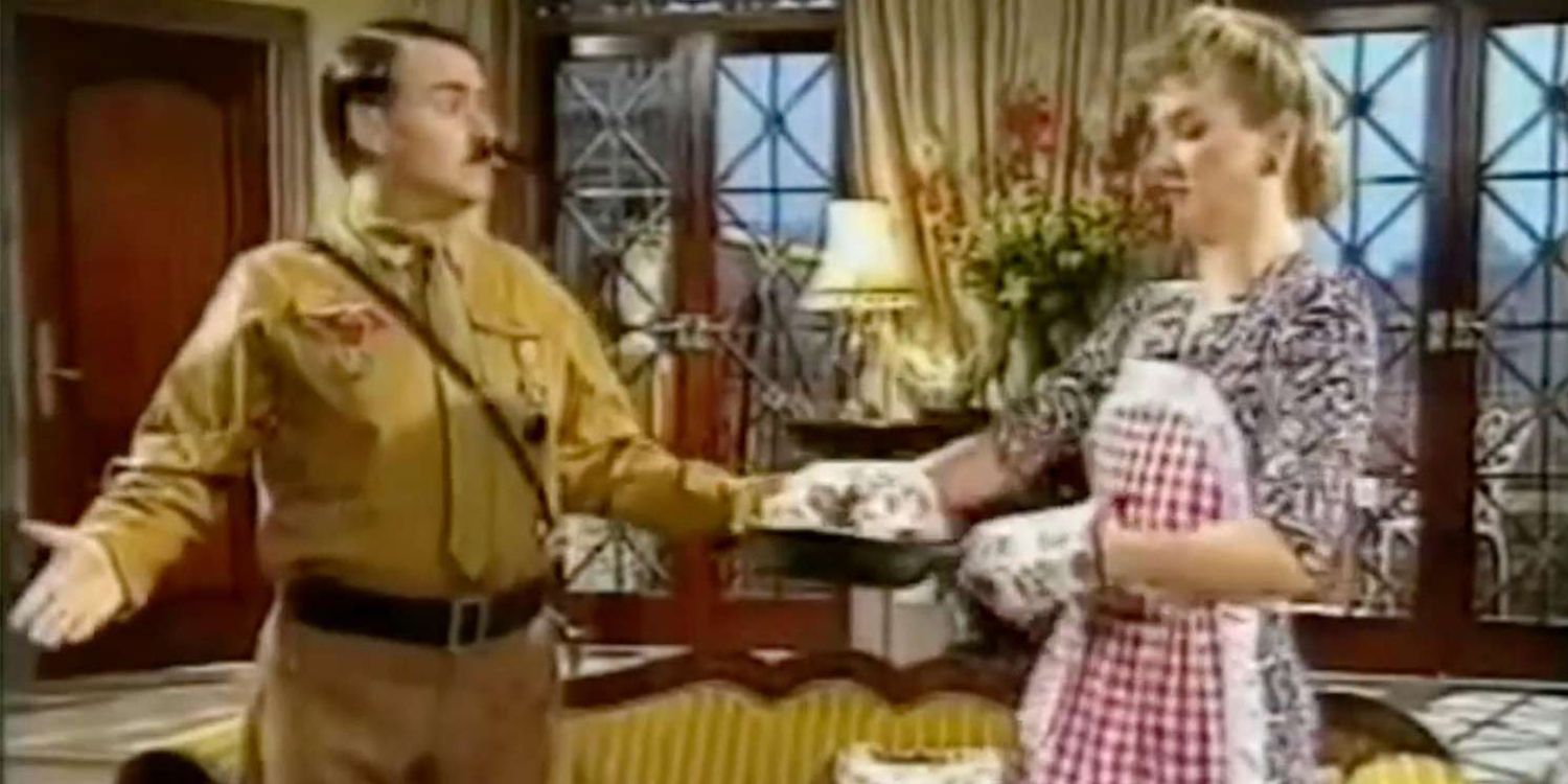 Neil McCaul as Adolf Hitler and DeNica Fairman as Eva Braun talking in the living room in Heil Honey, I'm Home!