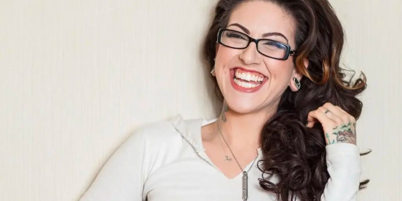 Olivia Black who was fired from Pawn Stars wearing white shirt and black rimmed glasses smiling wide in photo shoot