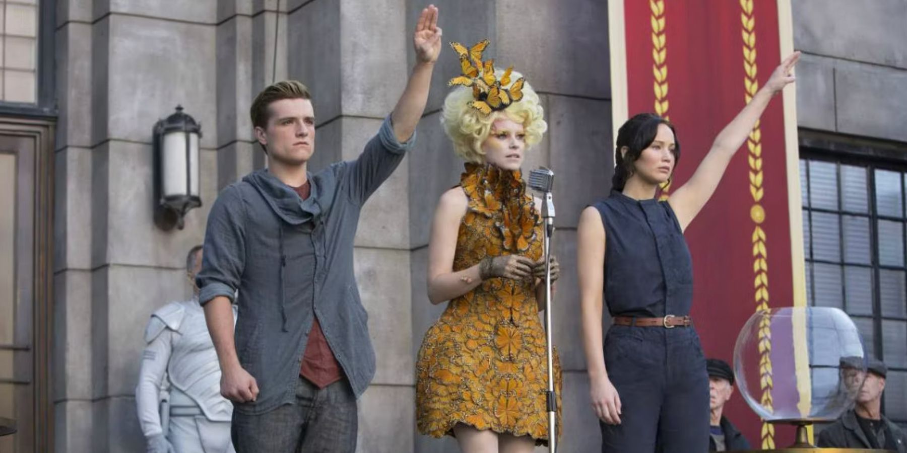 Peeta and Katniss giving the three finger salute while Effie speaks at the microphine in Hunger Games Catching Fire