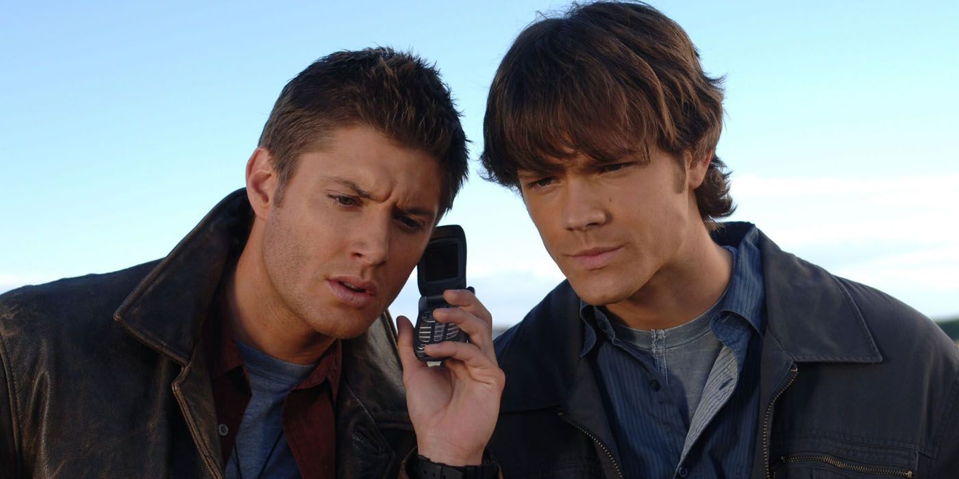 Jensen Ackles as Dean Winchester and Jared Padelecki as Sam Winchester intently listen to someone speaking on the phone in Supernatural