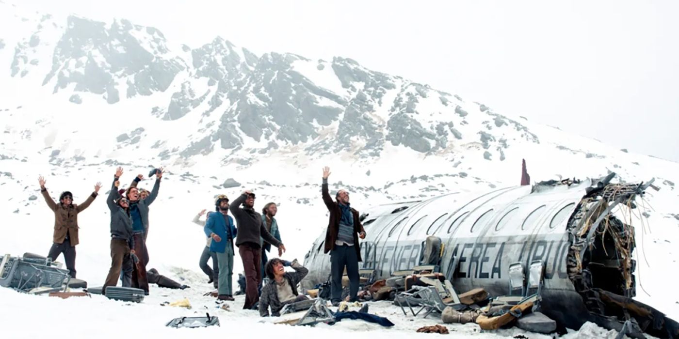 A group of survivors raise their arms around the fuselage of a crashed plane in the Andes mountains in Society of the Snow.