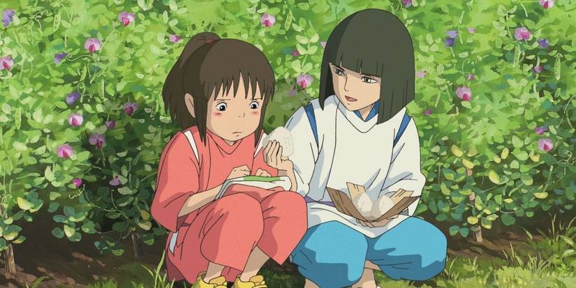 A boy hands a rice ball to a girl as they sit on the grass.