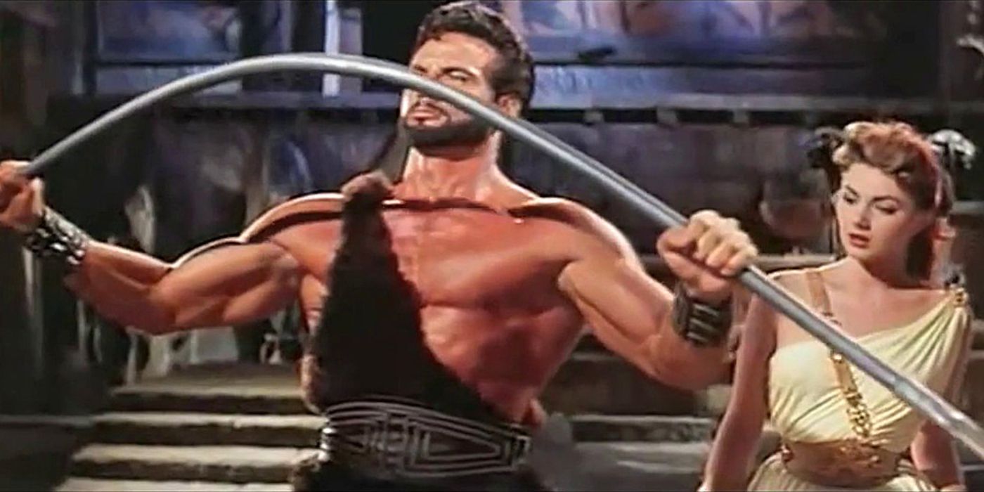 Steve Reeves as Hercules bending a metal bar as woman watches