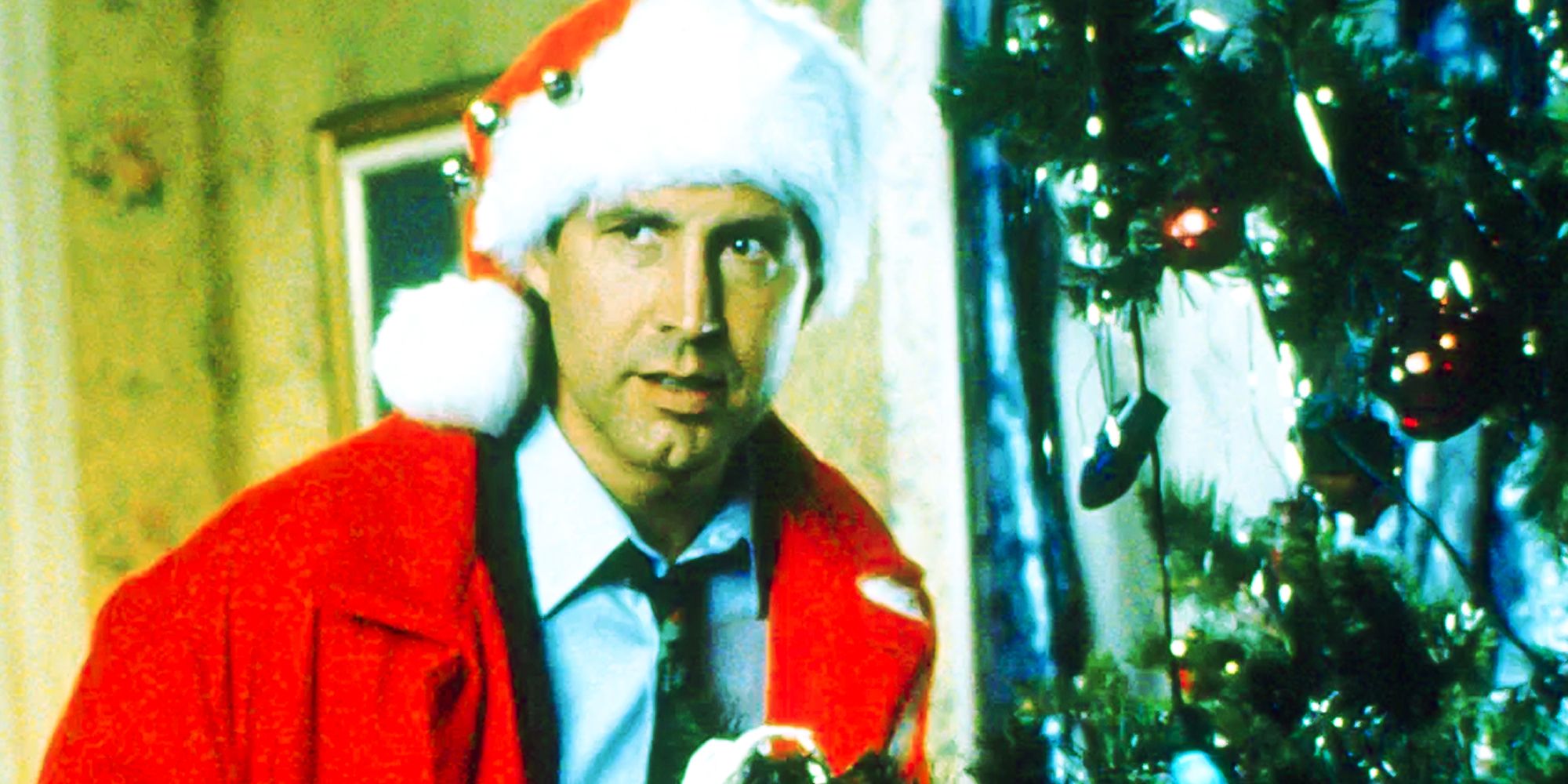 Chevy Chase as Clark Griswold wearing a Santa hat and standing next to the tree in Christmas Vacation (1989)