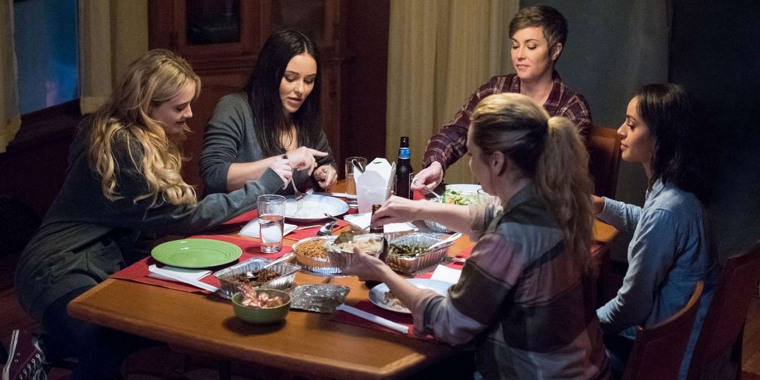 The cast of Supernatural's "Wayward Sisters" sitting around a table together eating and drinking
