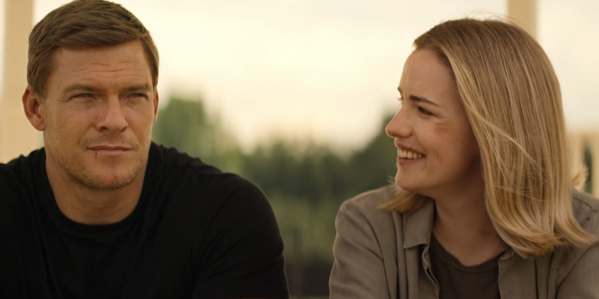 A smiling Willa Fitzgerald as Roscoe Conklin looking at Alan Ritchson as Reacher.