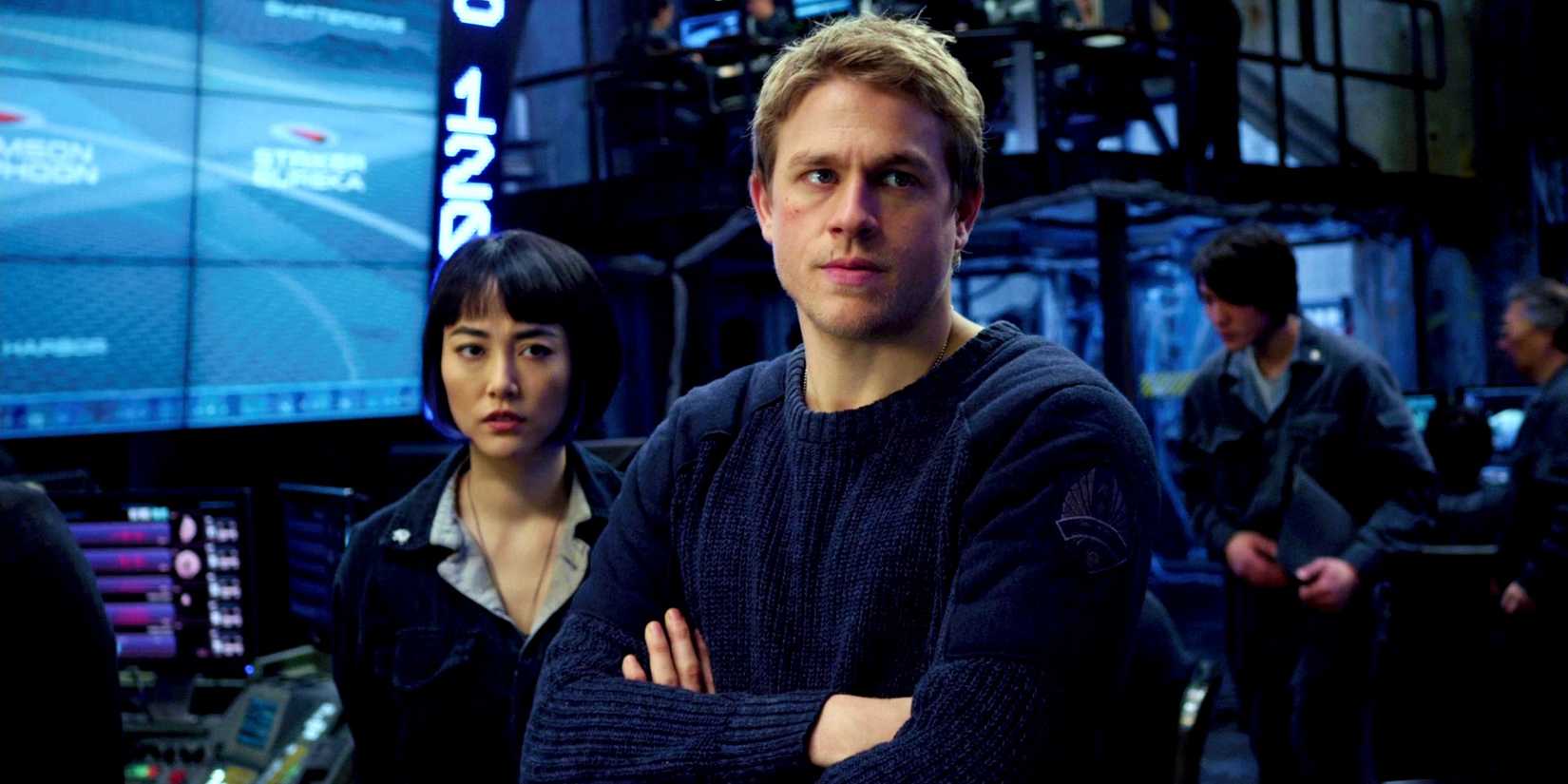 Charlie Hunnam as Raleigh folding his arm with Rinko Kikuchi's Mako behind him in Pacific Rim
