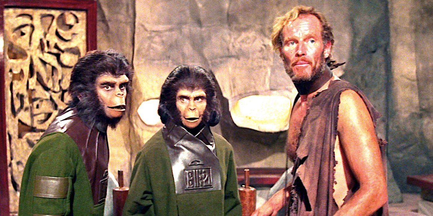 Charlton Heston's bedraggled George stands beside two apes indoors in Planet of the Apes 1968