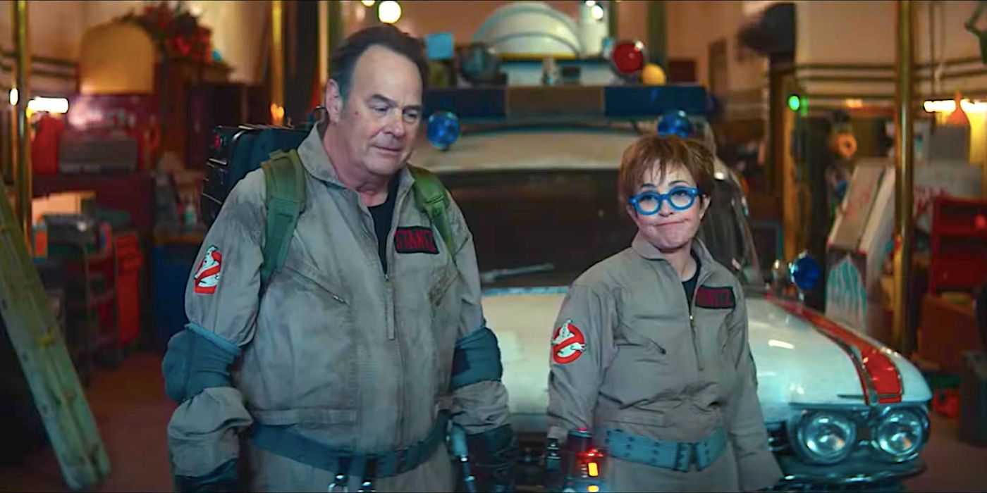 Dan Akroyd's Ray and Annie Potts' Janine looking resigned dressed as Ghostbusters in front of the Ecto-1 in Ghostbusters: Frozen Empire trailer