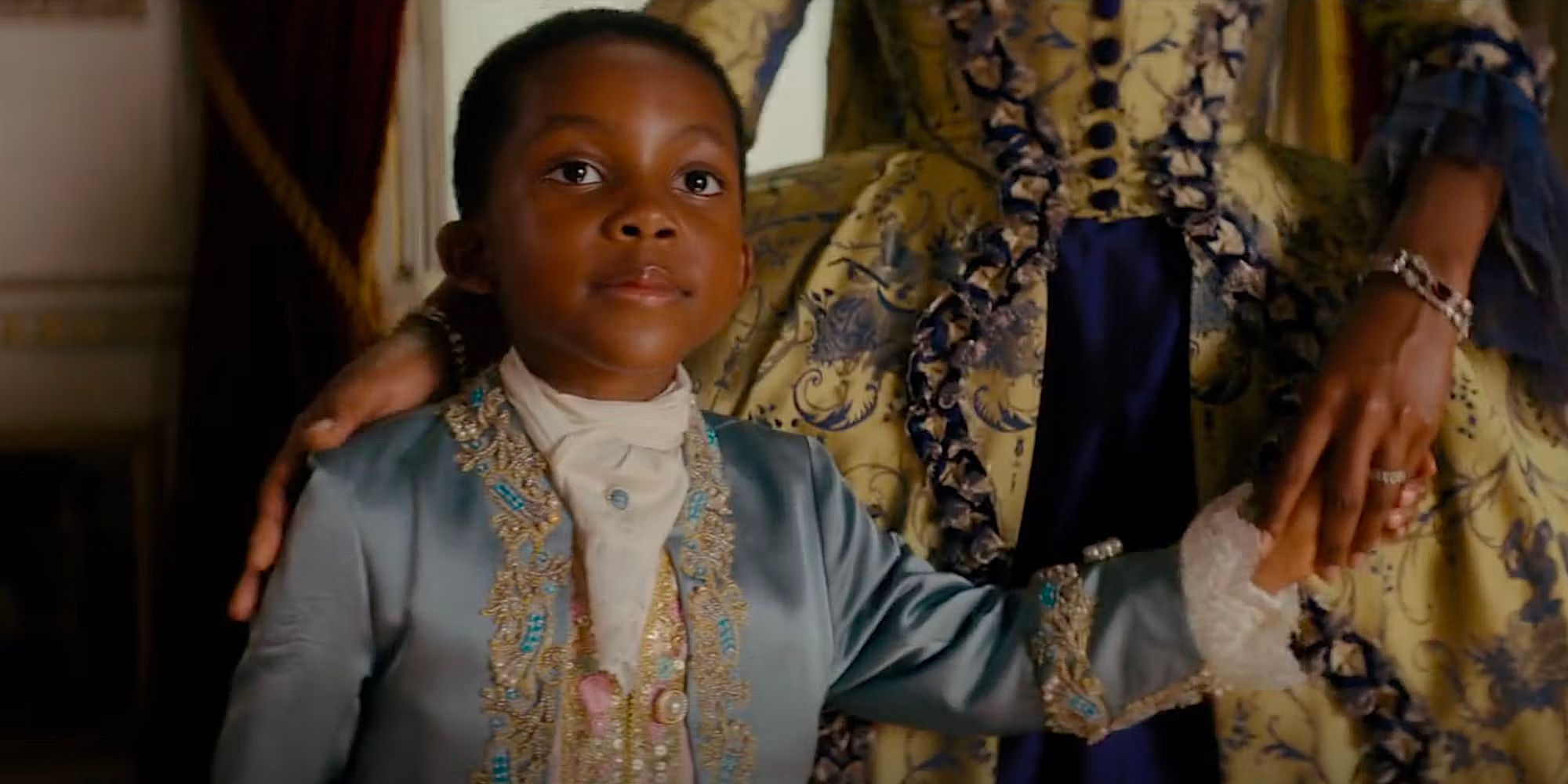 Isaiah Ajiboye as Dominic Danbury seated by his mostly unseen mother's side in Queen Charlotte: A Bridgerton Story