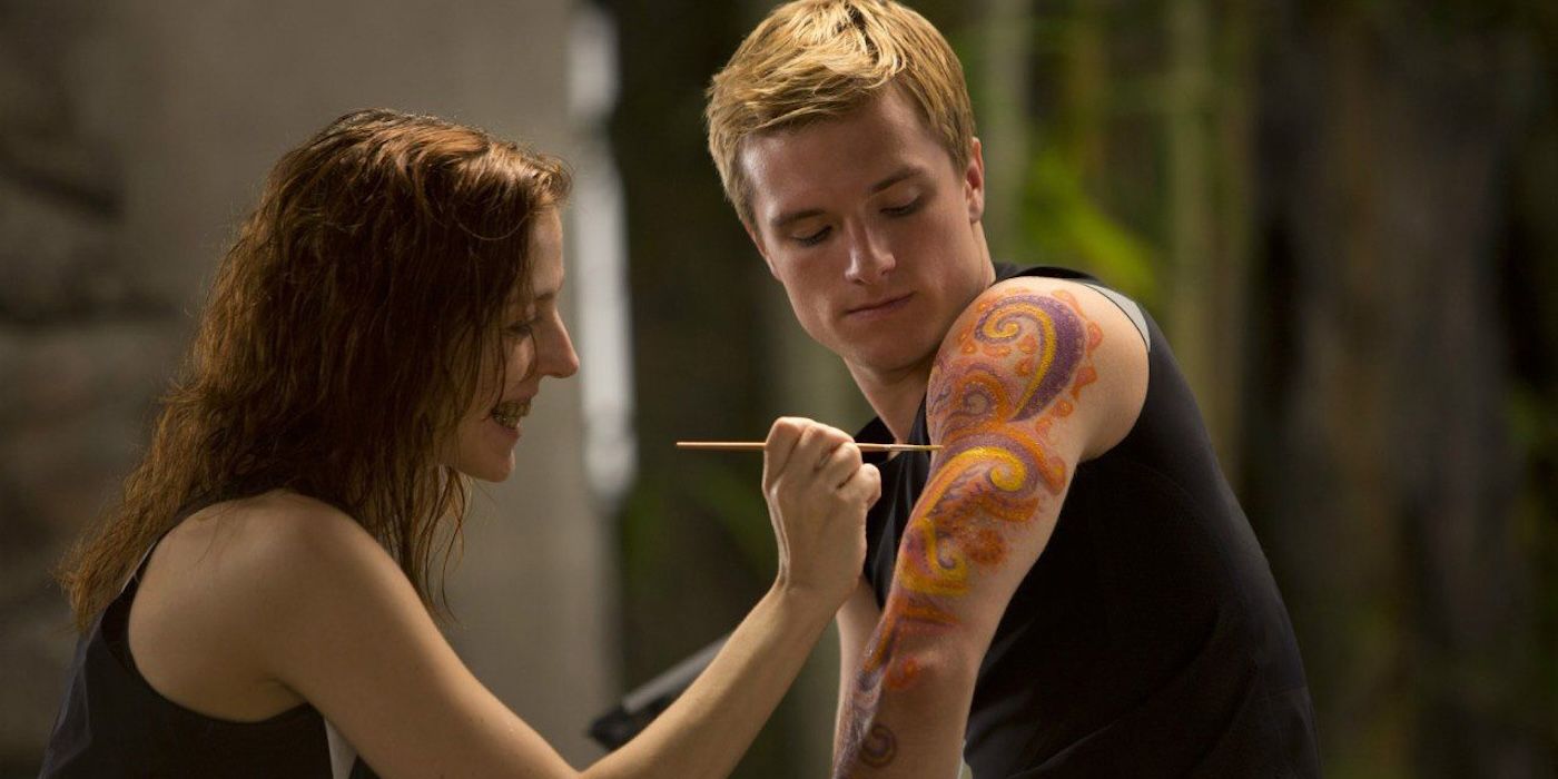 Female District 6 victory painting a design on Peeta's arm in the hunger games catching fire