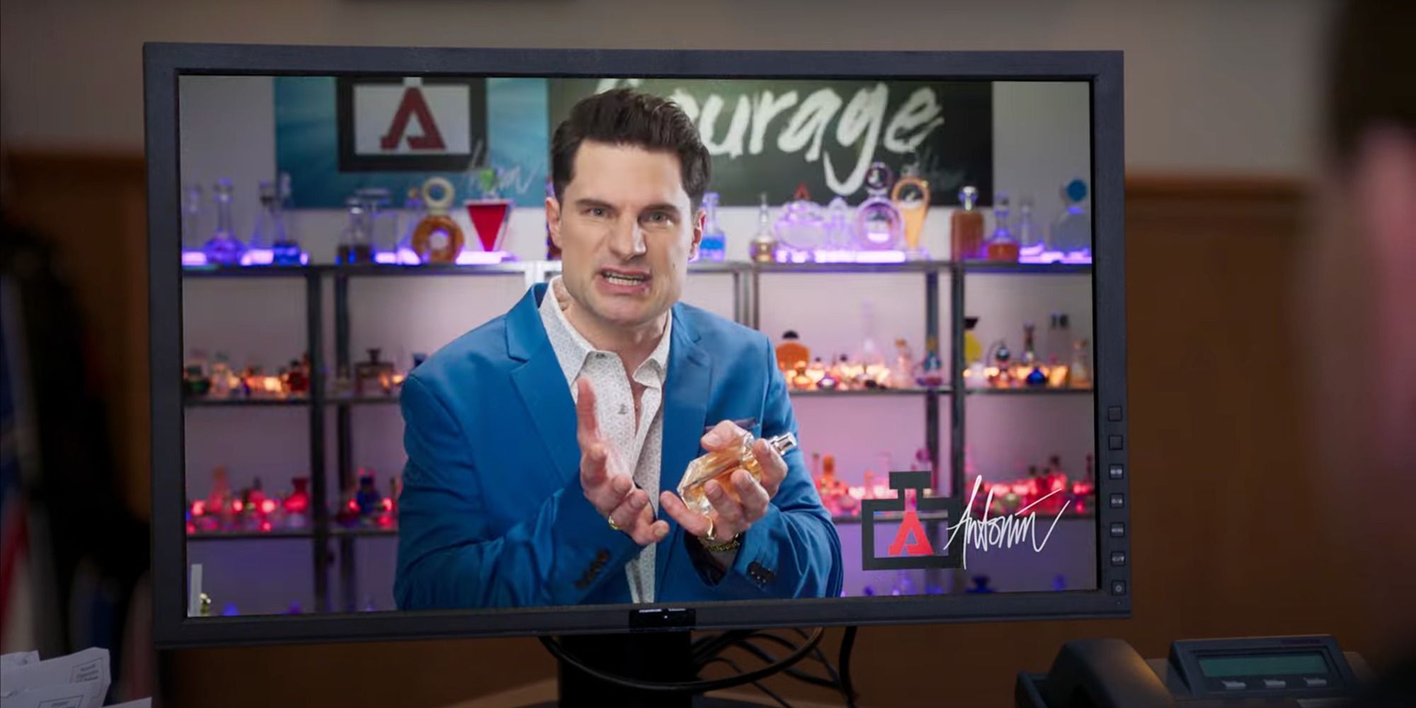 Flula Borg as Antonin Aroma holding up a bottle of perfume in Tacuma FD