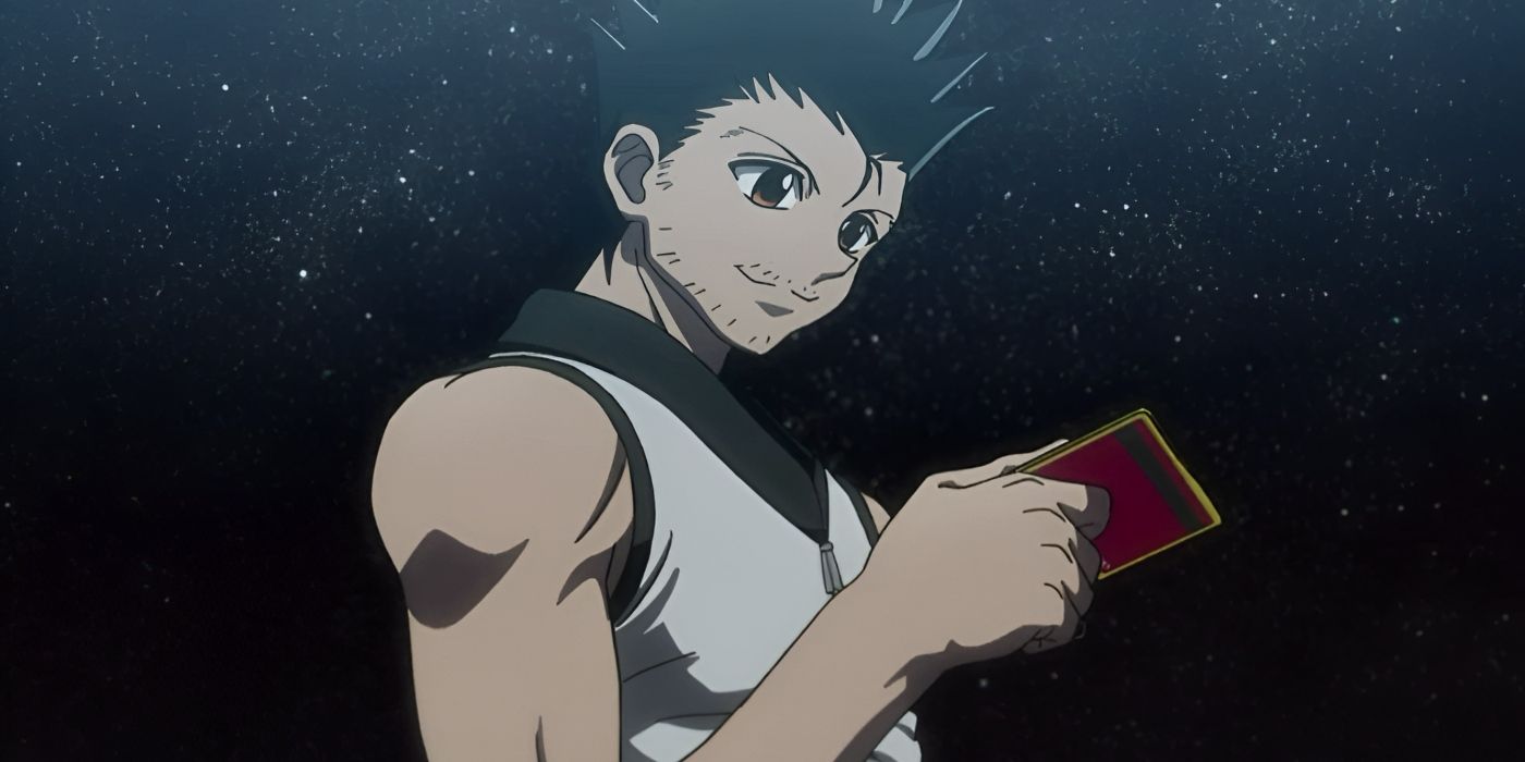 A man with spiky hair smiles as he looks at a card in his hand under the open sky.