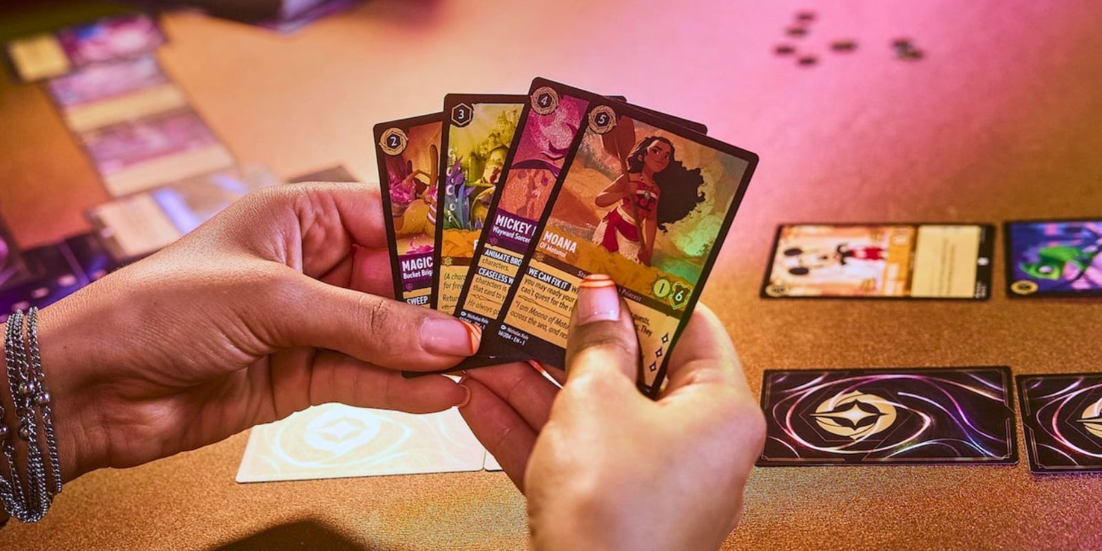 Hands holding some Disney Lorcana cards while playing the TCG