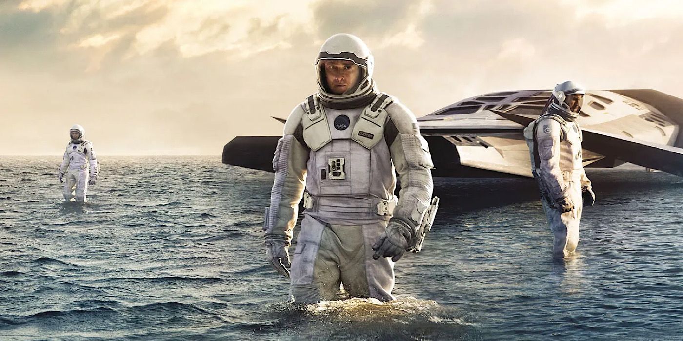 Para astronot berjalan di air dengan kapal di belakang mereka di Interstellar.
