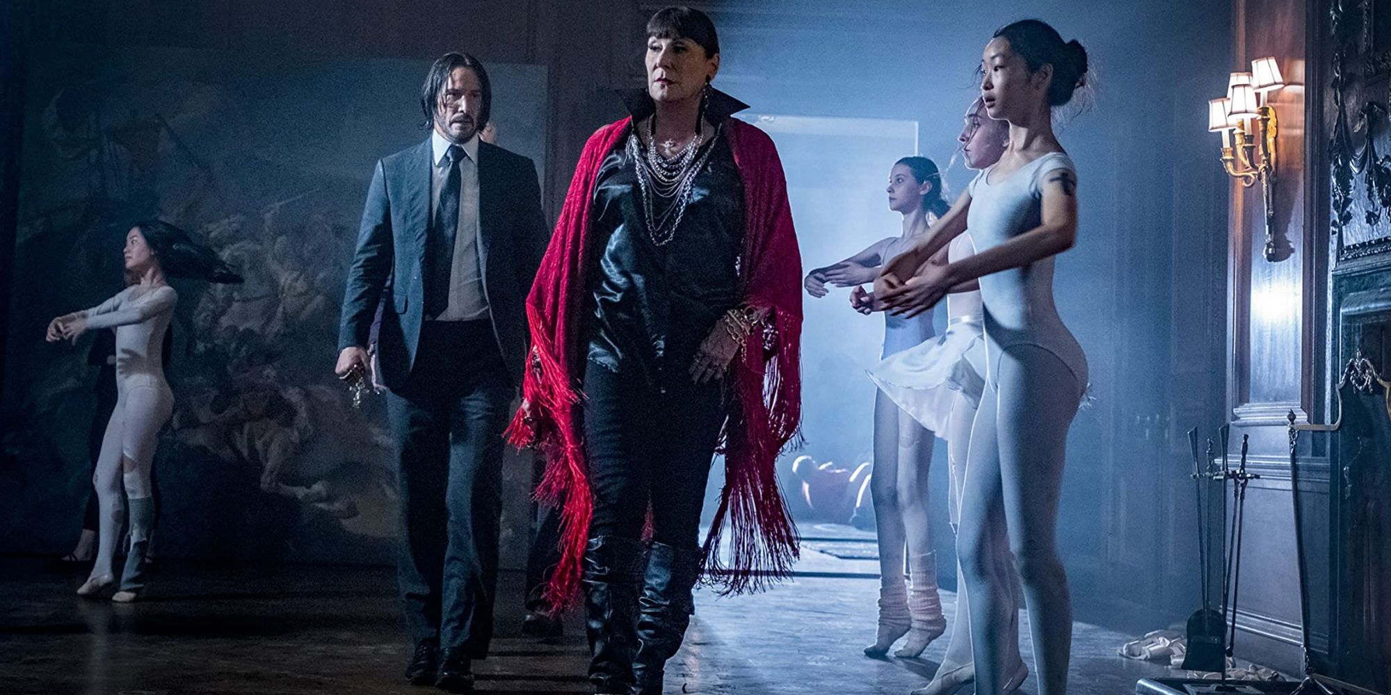 Keanu Reeves as John Wick and Anjelica Huston as The Director walk past ballerinas in John Wick: Chapter 3 - Parabellum.