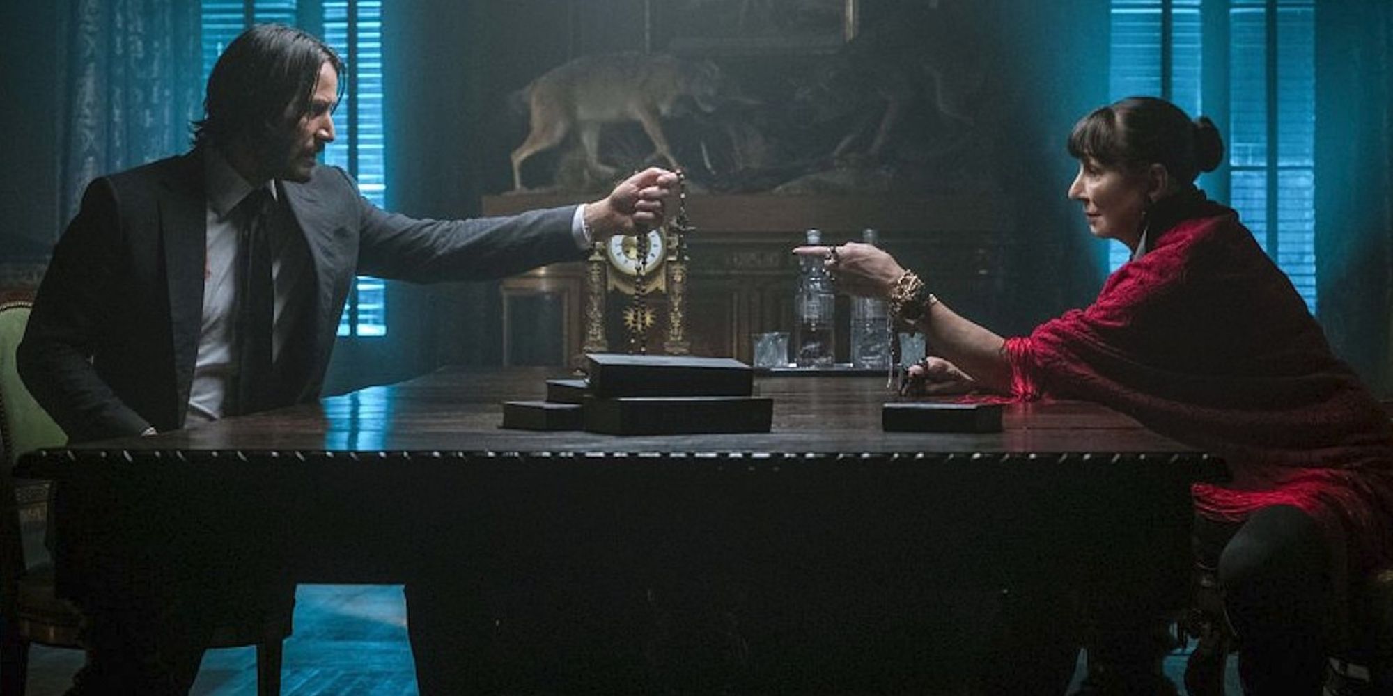 Keanu Reeves as John Wick holds up a gold cross to Anjelica Huston as The Director in John Wick: Chapter 3 - Parabellum.